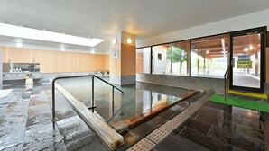 A hot spring bath area with a wooden bench, a glass barrier, and a view of the outside through large windows. - Hotel Marusansou (Chikuma)