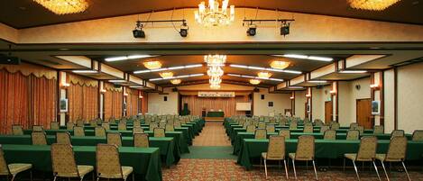 A conference room with rows of tables and chairs, a chandelier, and a stage with a banner.