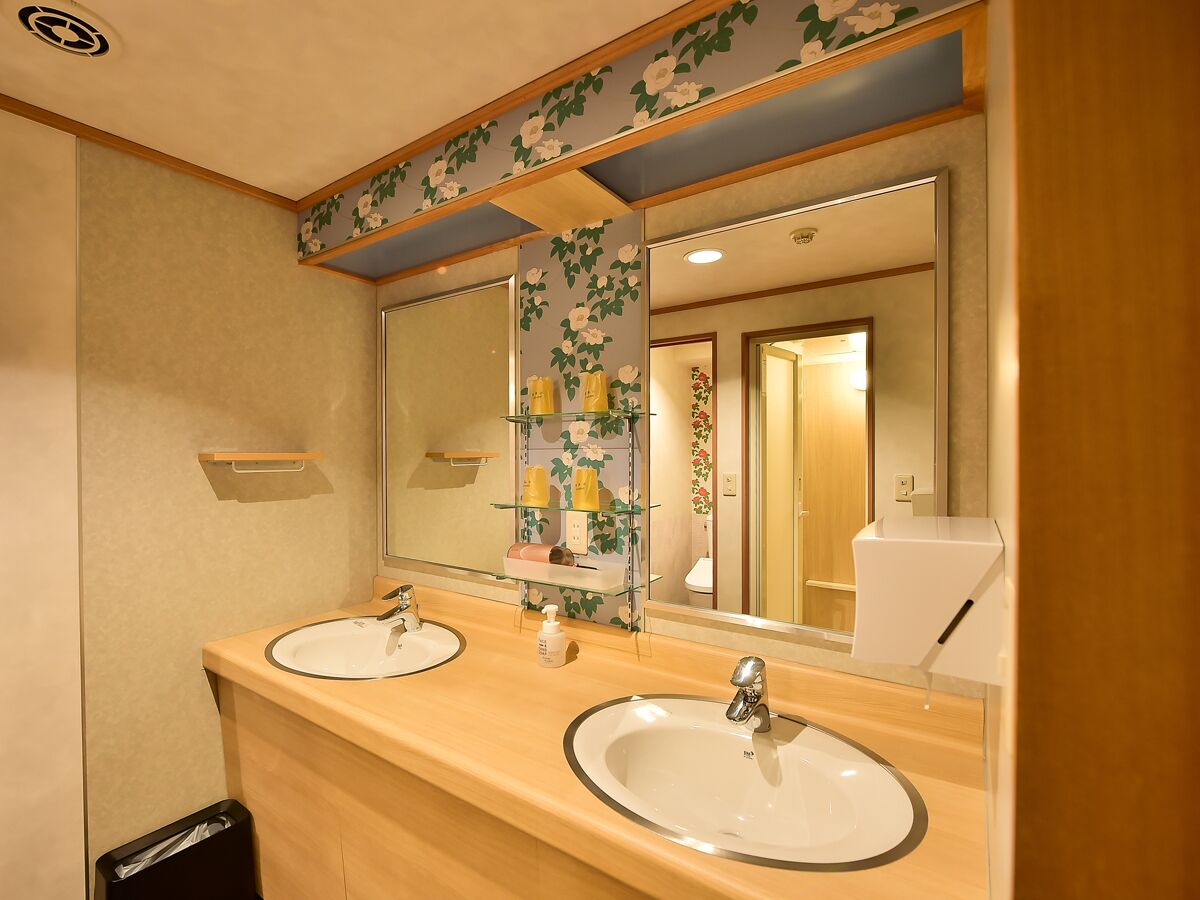 A bathroom with two sinks, a mirror, and a shelf with toiletries.