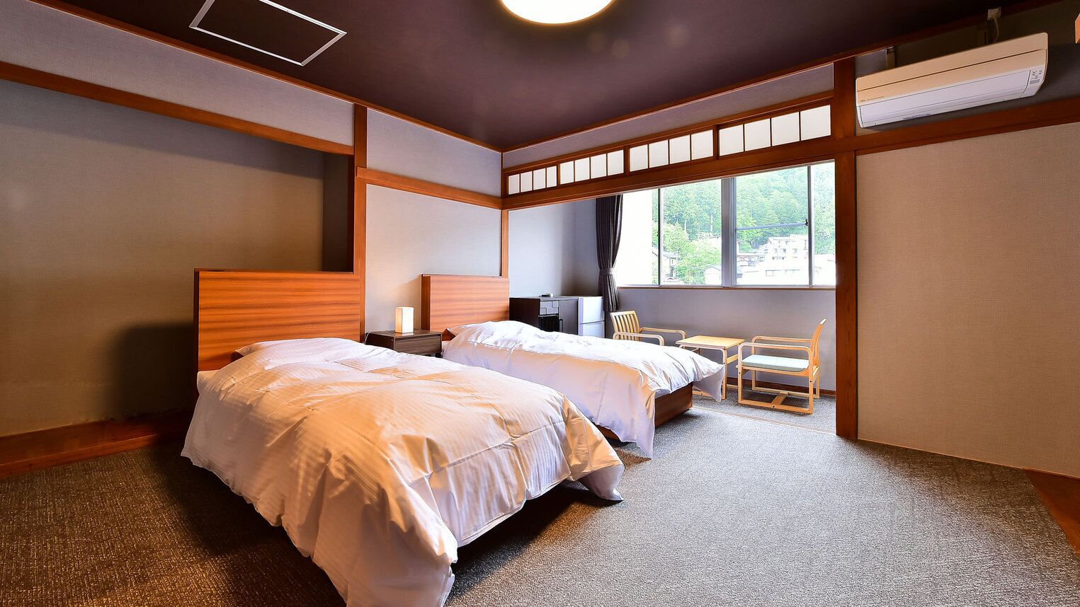 Ein Hotelzimmer mit zwei Betten, einem Schreibtisch, Stühlen und einem großen Fenster.