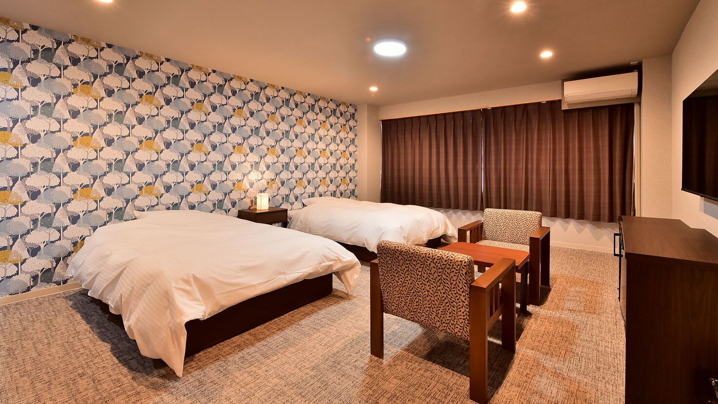 Ein Hotelzimmer mit zwei Betten, einem Schreibtisch, einem Sessel, einem Fernseher und einer Wand mit Muster.