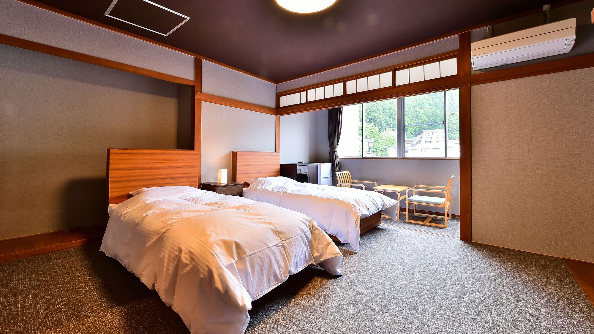 Ein Hotelzimmer mit zwei Betten, einem Schreibtisch, einem Stuhl und einem großen Fenster.