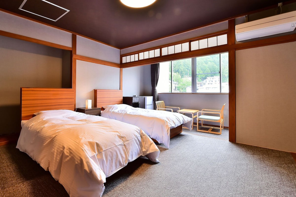 Ein Hotelzimmer mit zwei Betten, einem Schreibtisch, einem Stuhl und einem großen Fenster.