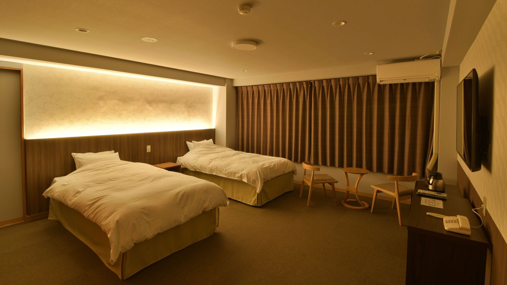 Ein Hotelzimmer mit zwei Betten, einem Schreibtisch, einem Sessel, einem Fernseher und einer Klimaanlage.
