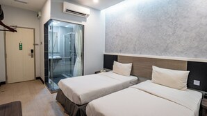 A hotel room with two beds, a glass shower enclosure, a wooden headboard, and a door with a green sign. - Indra Hotel (Ipoh)