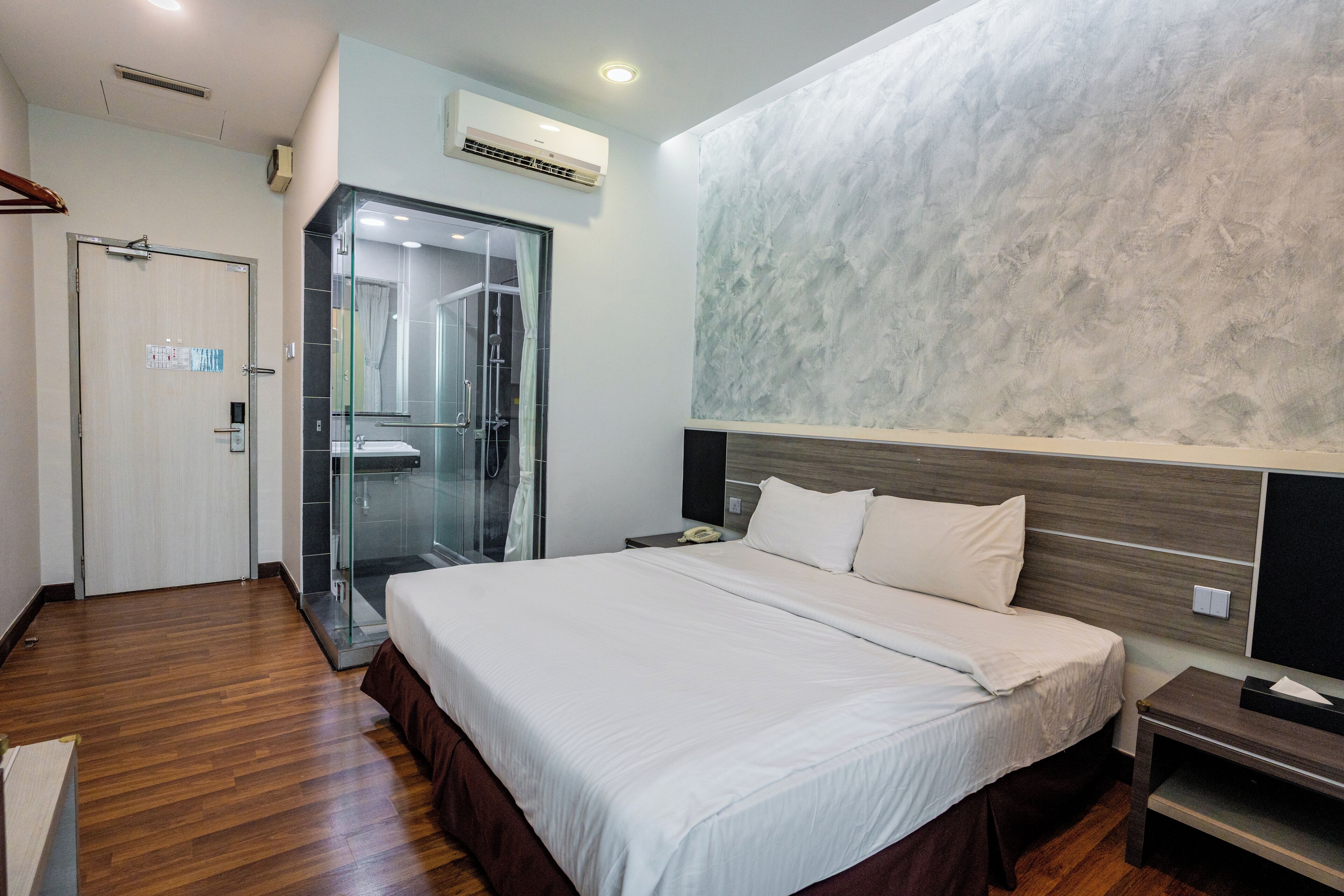 A modern hotel room with a large bed, a glass shower enclosure, and a wooden floor.