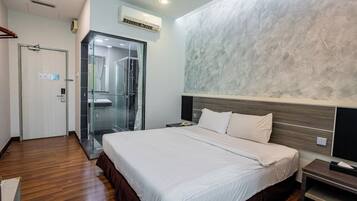 A modern hotel room with a large bed, a glass shower enclosure, and a wooden floor.