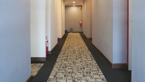 A hotel hallway with a patterned carpet, white walls, and a fire extinguisher on the left. - Indra Hotel (Ipoh)