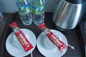 Two white plates with a packet of Gold Roast coffee mix on each. Behind the plates, there are two bottles of water and a stainless steel coffee pot. - Indra Hotel (Ipoh)