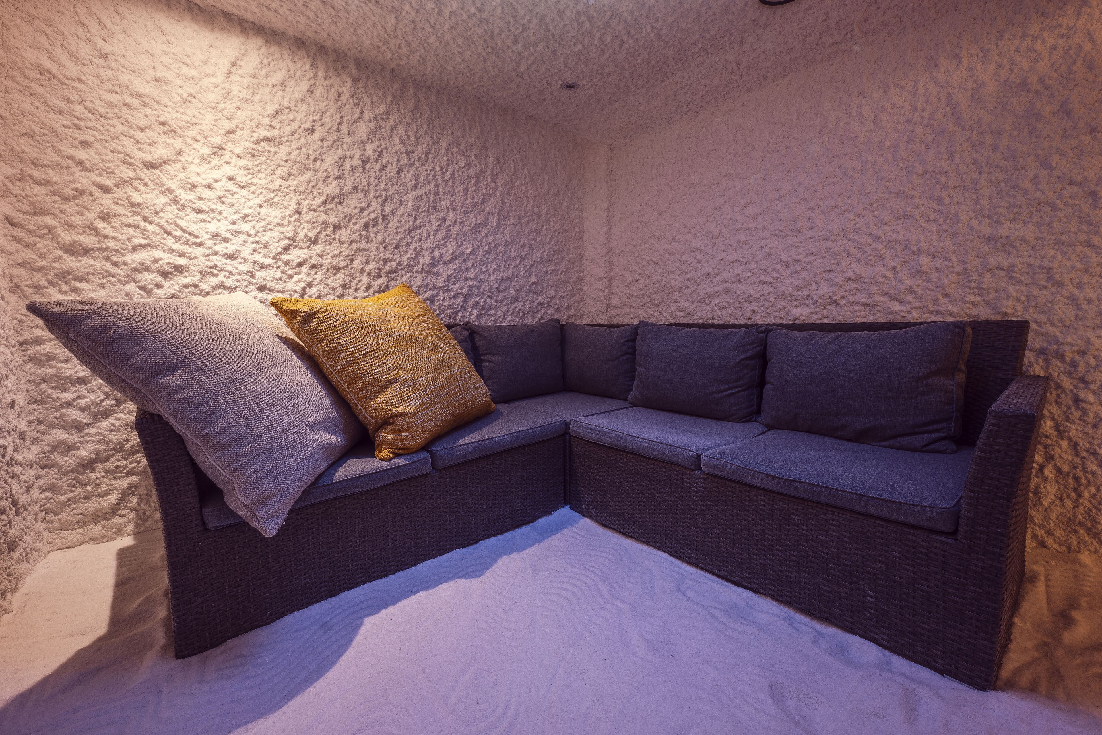A corner sofa with cushions, a textured wall, and a white carpet.
