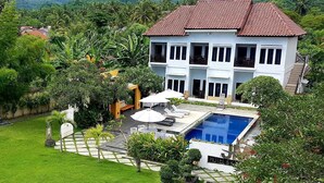 Un hotel de dos pisos con piscina, rodeado de exuberante vegetación y un paisaje montañoso.