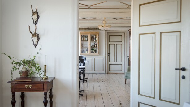 A room with a wooden floor, a desk with a plant, a cabinet with glass doors, and a door with gold trim. - Pension Holmegaard (Allinge)
