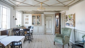 A dining area with a table and chairs, a chandelier, and a cabinet with glass doors. - Pension Holmegaard (Allinge)
