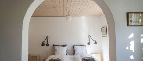 Una habitación con dos camas, techo de madera y un arco blanco.
