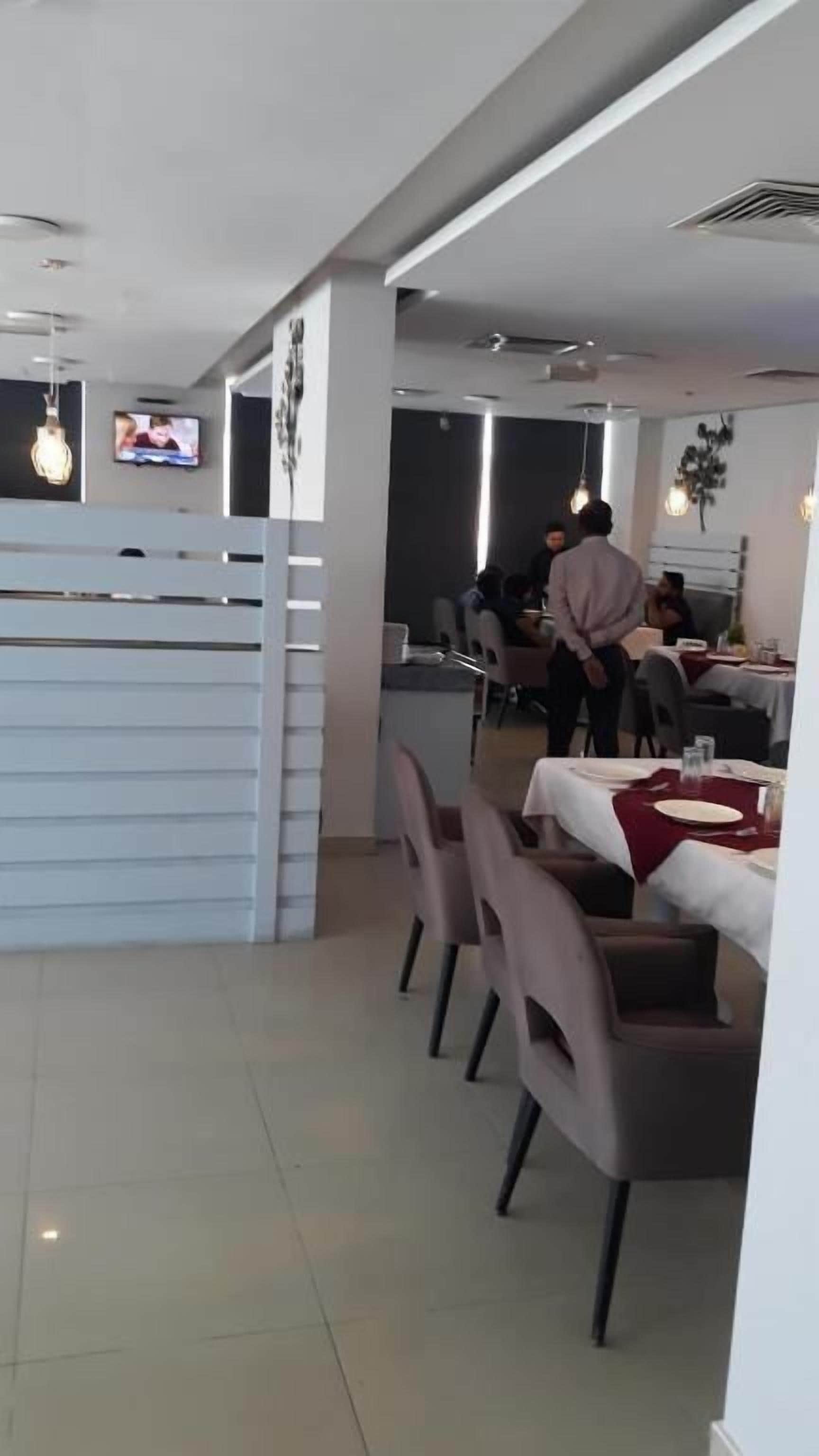 A restaurant with tables and chairs, a TV screen, and a person in the background.