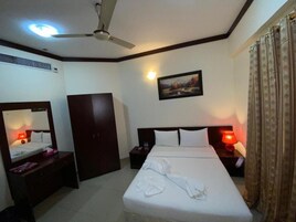 A hotel room with a bed, a wardrobe, a nightstand, a bedside table, a ceiling fan, and a painting on the wall.