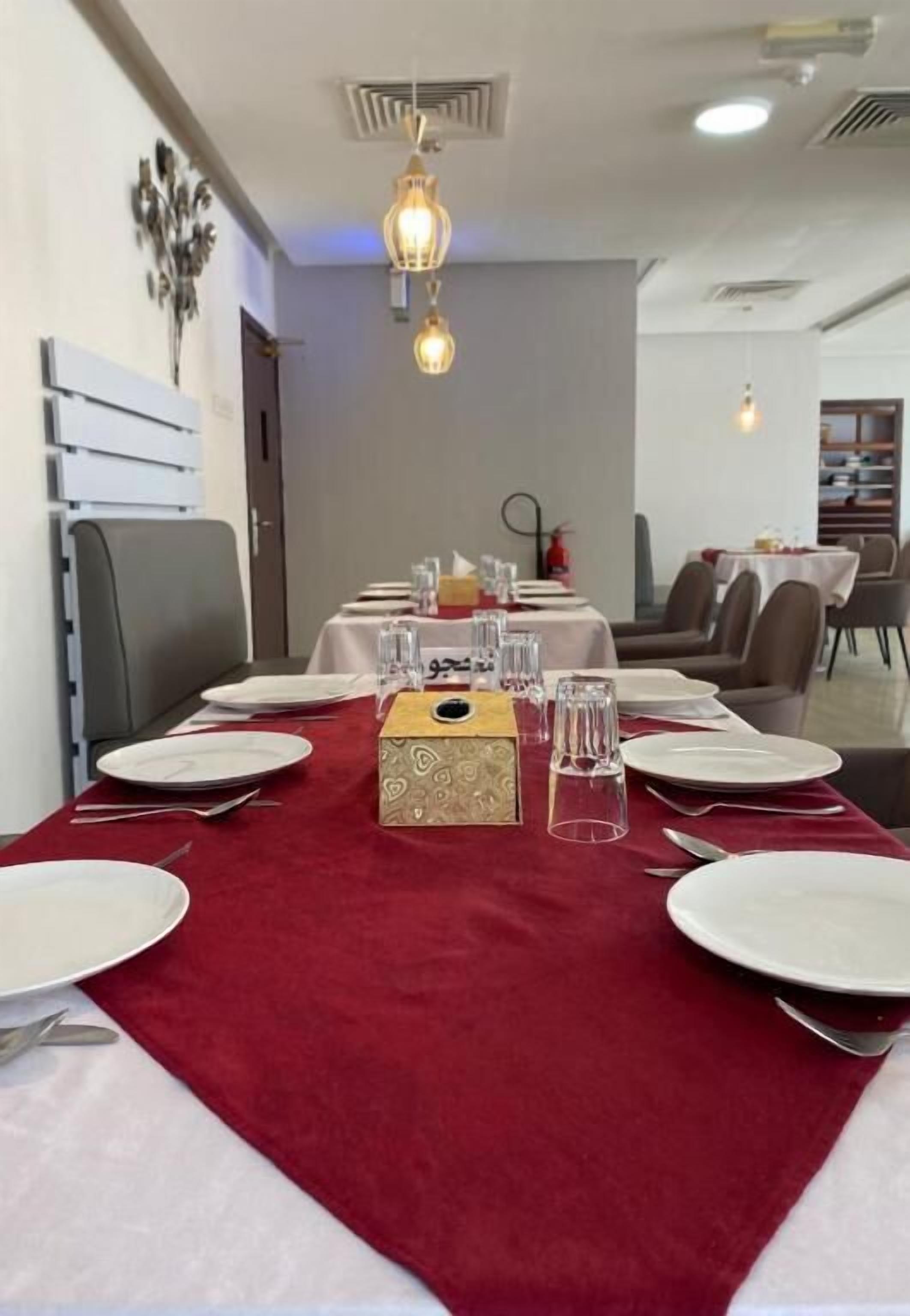 Uma área de refeições com toalha de mesa vermelha, pratos brancos e copos de vidro dispostos para uma refeição.
