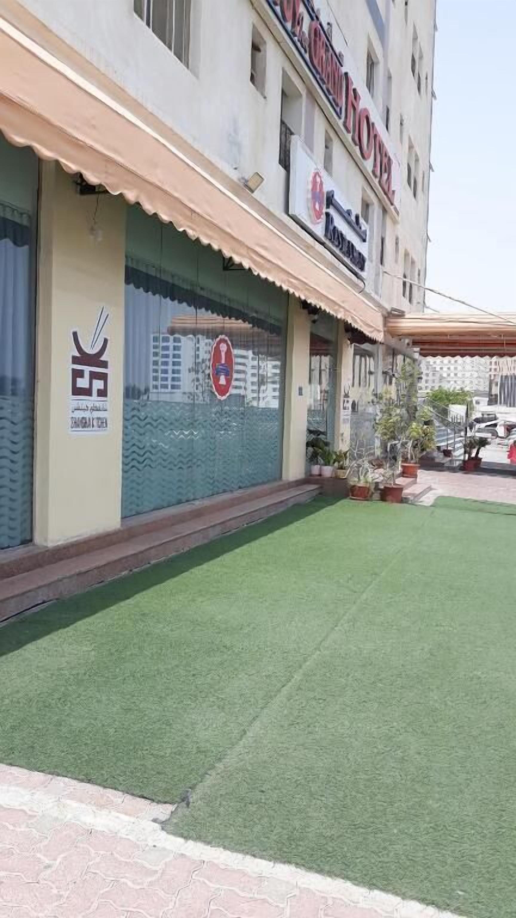 A hotel with a green lawn in front, a signboard with the hotel's name, and a parking area with cars.