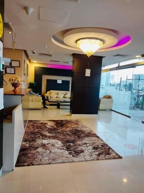 A hotel lobby with a chandelier, a reception desk, a sofa, and a large rug. - Savoy Grand Hotel Apartments (Muscat)