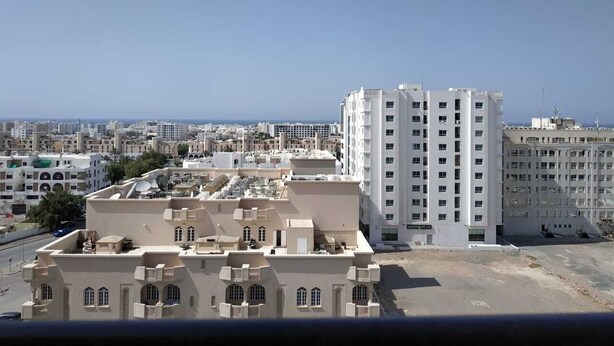A cityscape with a prominent white high-rise building in the center. - Savoy Grand Hotel Apartments (Muscat)