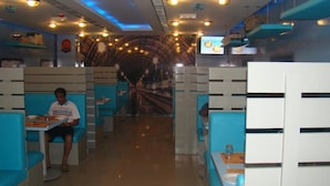 A restaurant with booths and tables, a curved ceiling, and a television screen. - Savoy Grand Hotel Apartments (Muscat)