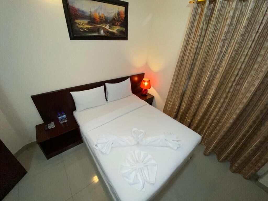 A hotel room with a neatly made bed, a nightstand with a lamp, and a painting on the wall.