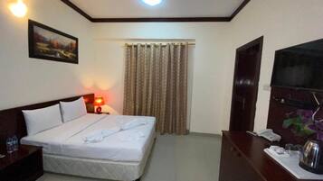 Una habitación de hotel con cama, escritorio, teléfono, un cuadro en la pared y ventilador de techo.