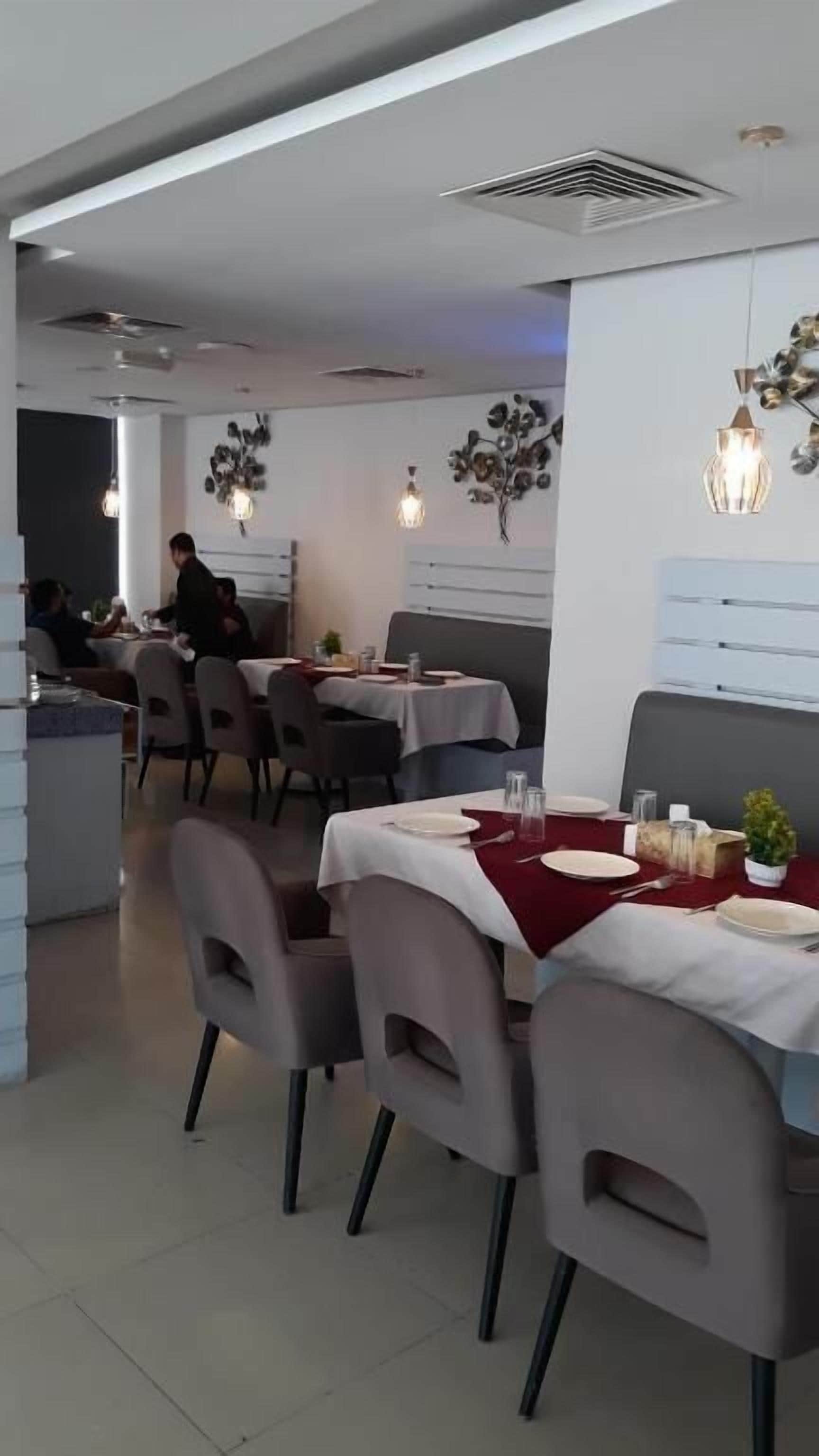 A restaurant interior with tables set for dining, a person seated at a table, and decorative wall art.
