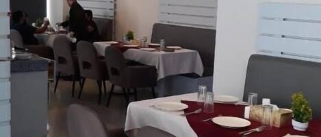 A restaurant interior with tables set for dining, a person seated at a table, and decorative wall art.