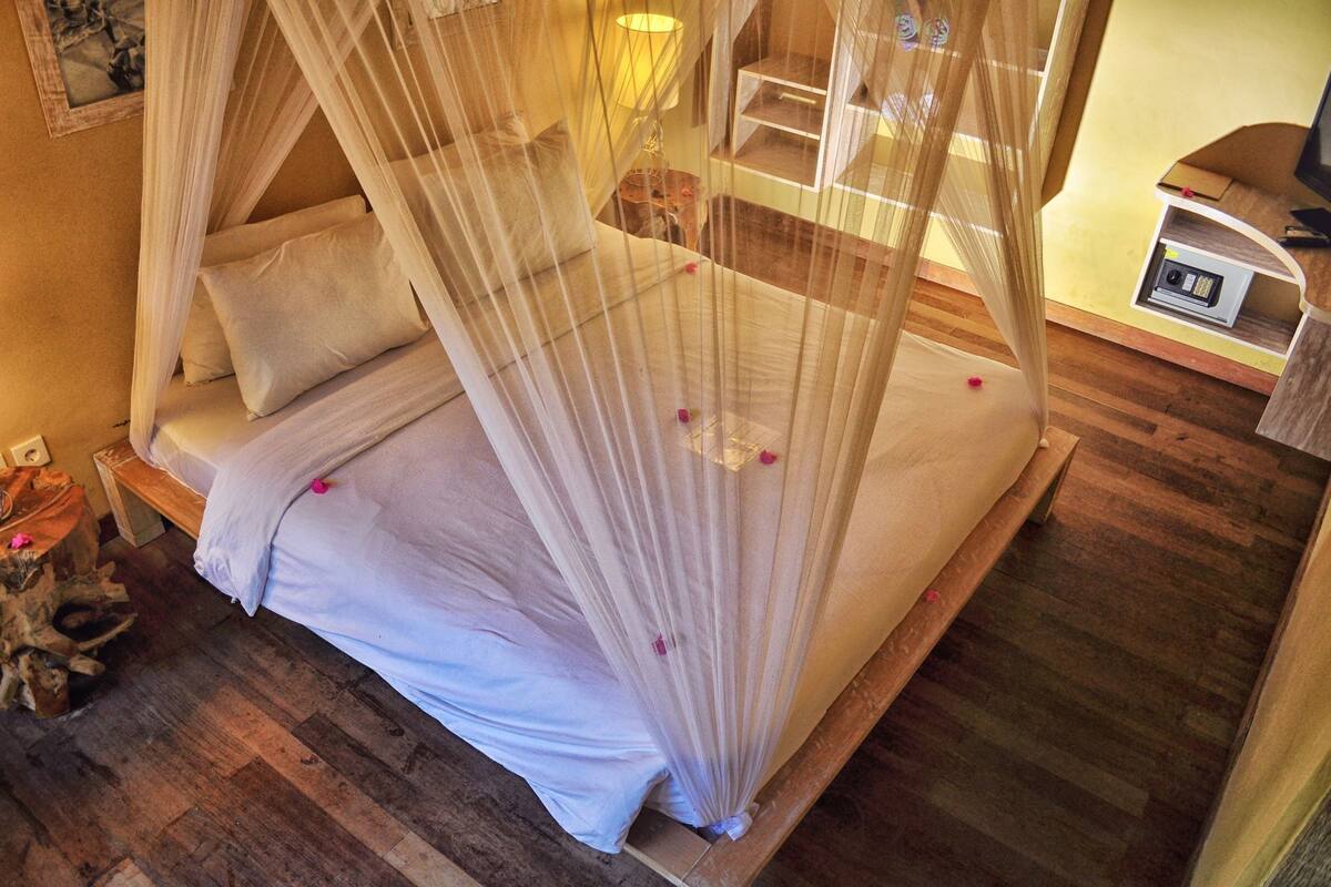 Ein Zimmer mit einem Bett unter einem Baldachin, einem Nachttisch, einer Lampe und einem kleinen Tisch mit einem Gerät darauf.