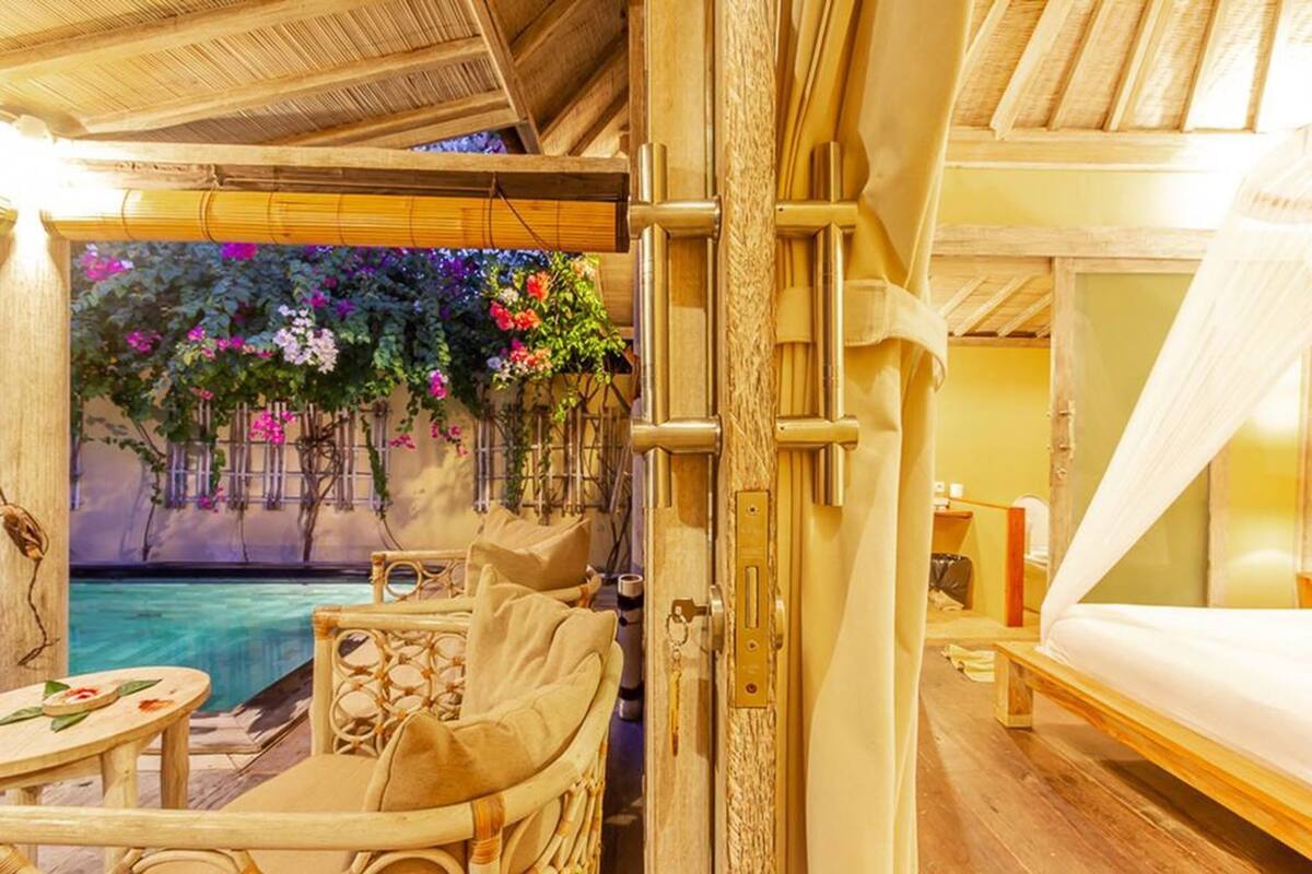 A room with a bed, a small table, a chair, and a view of a pool with flowers.