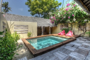 Piscina con cubierta de madera, rodeada por una estructura de techo de paja y abundante vegetación.