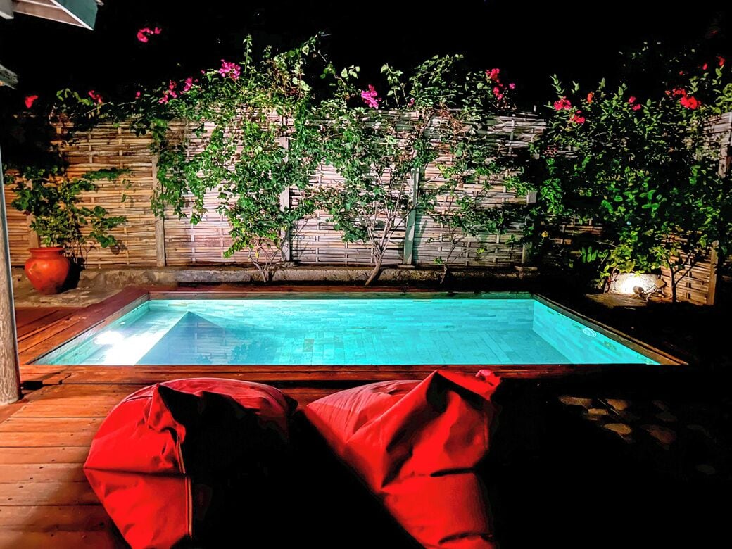 A swimming pool with wooden deck seating and a bamboo fence with flowering plants.
