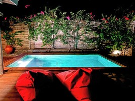 Una piscina con solárium de madera, asientos y valla de bambú con plantas en flor.