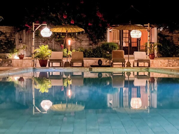 Un área junto a la piscina con sillones de descanso, sombrillas y plantas en macetas.