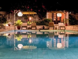 A poolside area with lounge chairs, umbrellas, and potted plants.