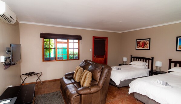 Habitación de hotel con un sillón de cuero, dos camas, un televisor y una ventana con vista a zonas verdes.