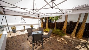 Eine Terrasse im Freien mit Tisch und Stühlen, einem weißen Sonnenschirm und einem Holzzaun.