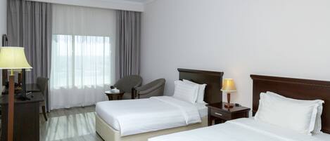 Habitación de hotel con dos camas, un escritorio, una silla y una lámpara.