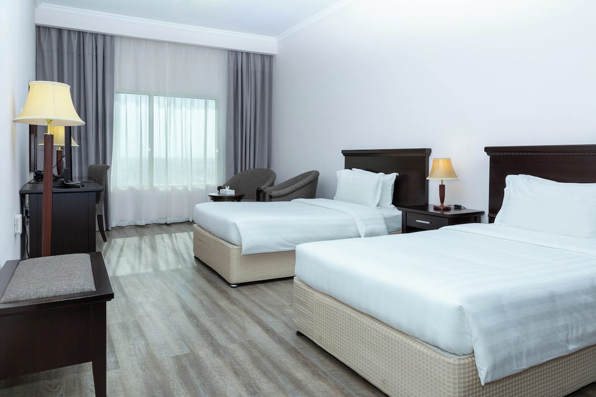 A hotel room with two beds, a desk, a chair, and a lamp.