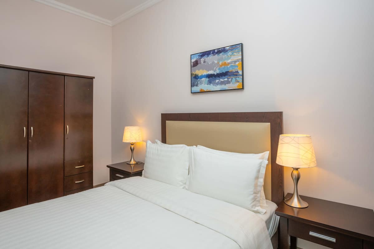 A hotel room with a large bed, two bedside tables with lamps, a wardrobe, and a painting on the wall.