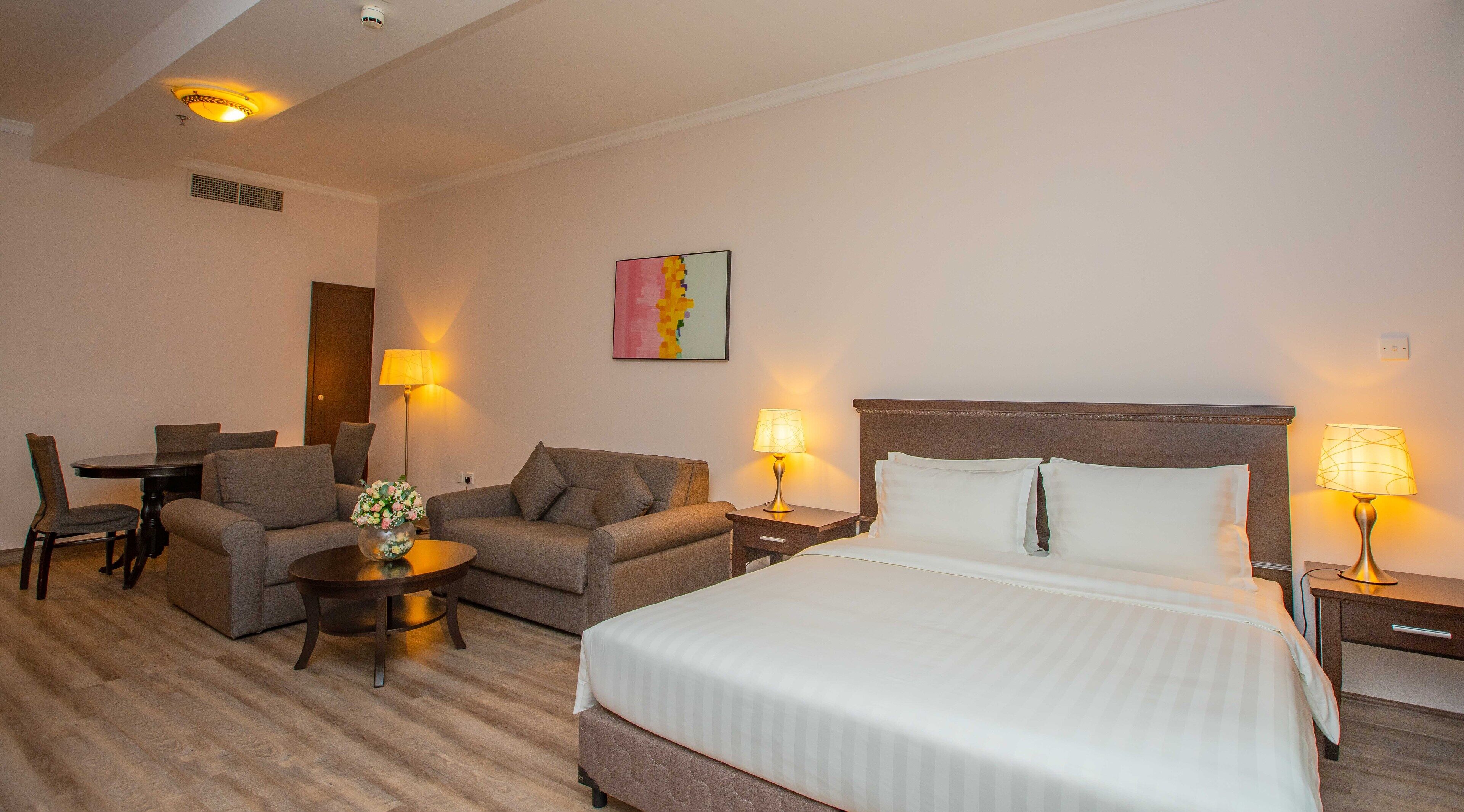 A hotel room with a bed, two sofas, a dining table with chairs, and two bedside lamps.