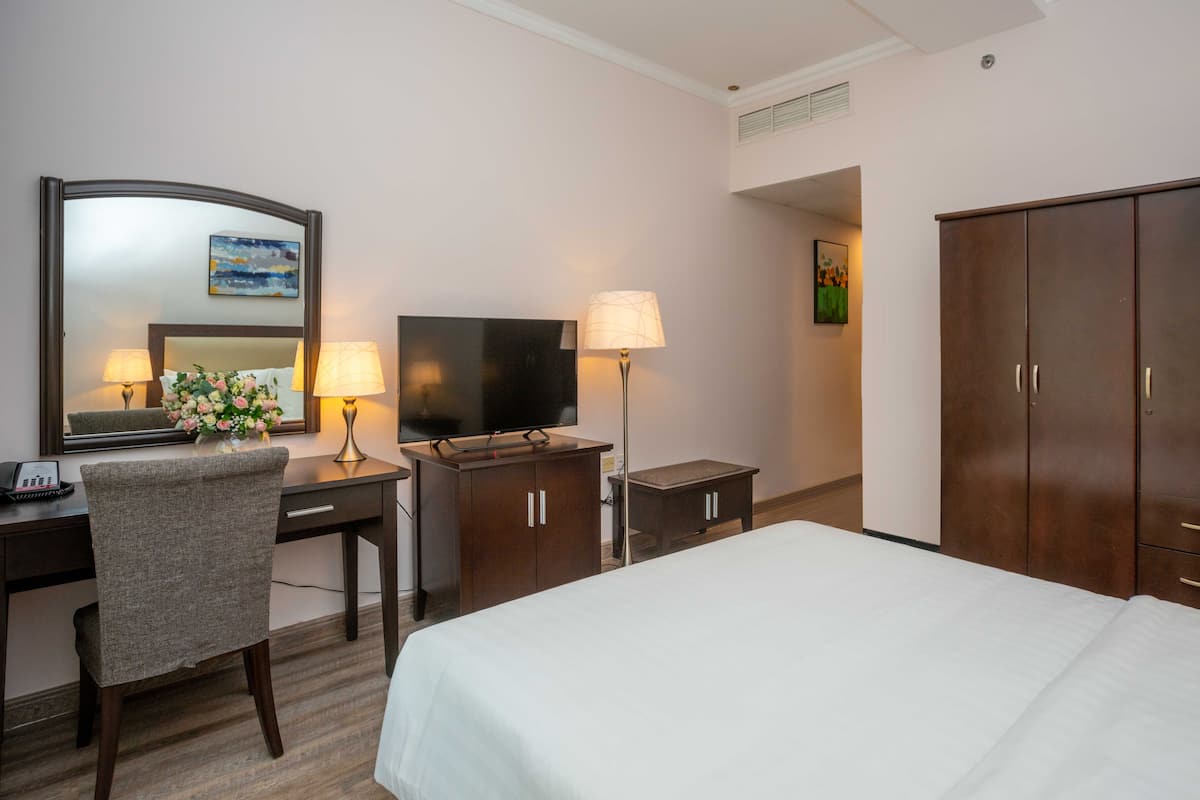 A hotel room with a bed, desk, chair, TV, lamp, and wardrobe.