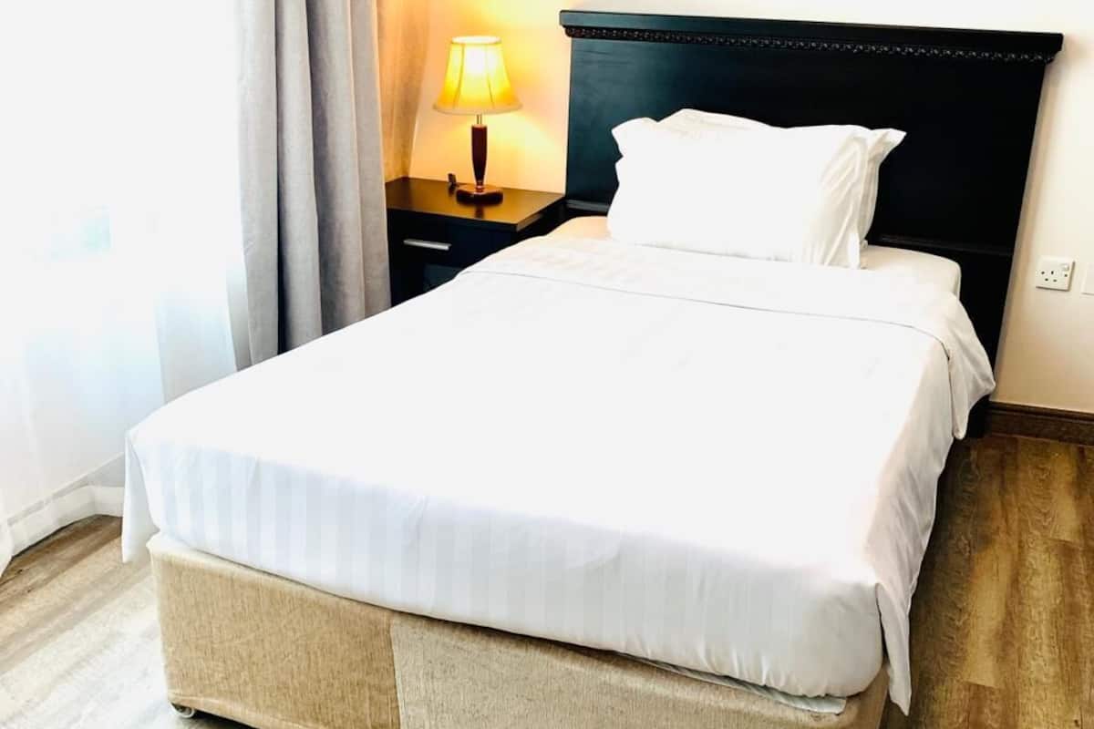 A neatly made bed with white linens, a dark headboard, and a bedside lamp.