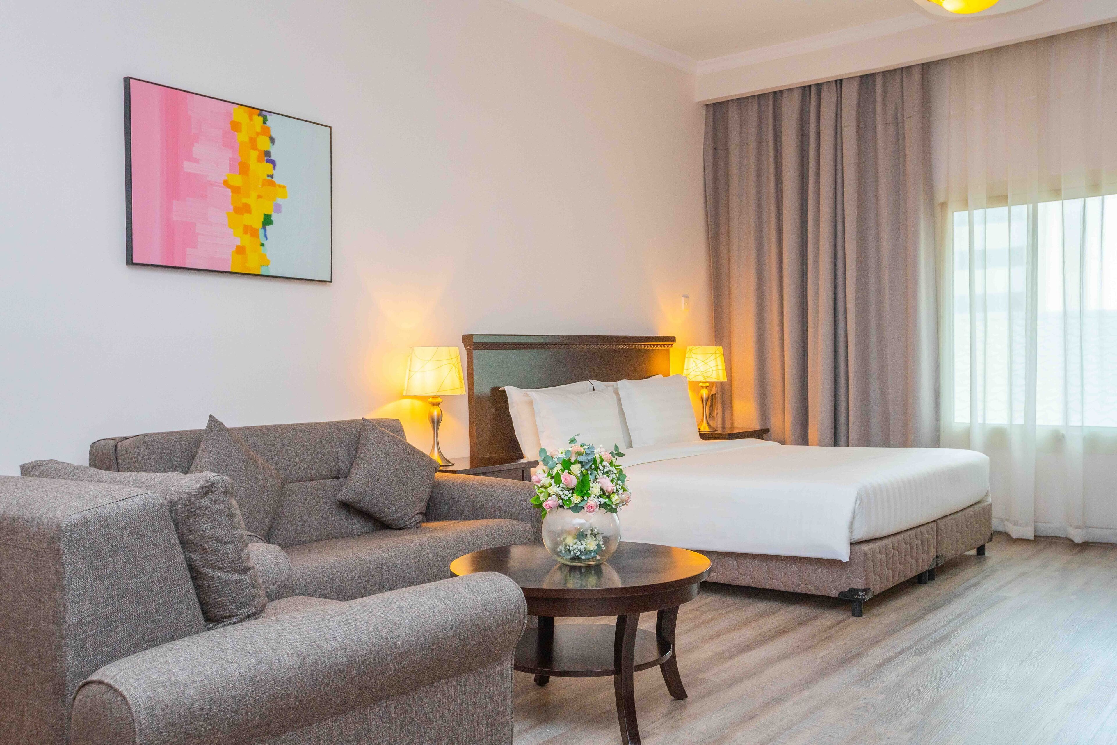 Ein Hotelzimmer mit einem Bett, einem Sofa, einem kleinen Tisch mit einer Vase und einem Bild an der Wand.