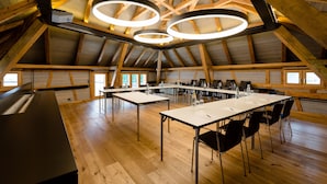 A spacious room with a high wooden ceiling, multiple tables, and chairs arranged for meetings. - Hotel Krone Speicher (Speicher)