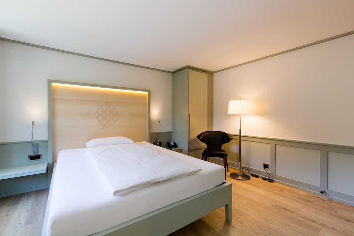 Un lit bien fait dans une chambre d’hôtel, avec une tête de lit, une table de chevet, une lampe et une chaise.