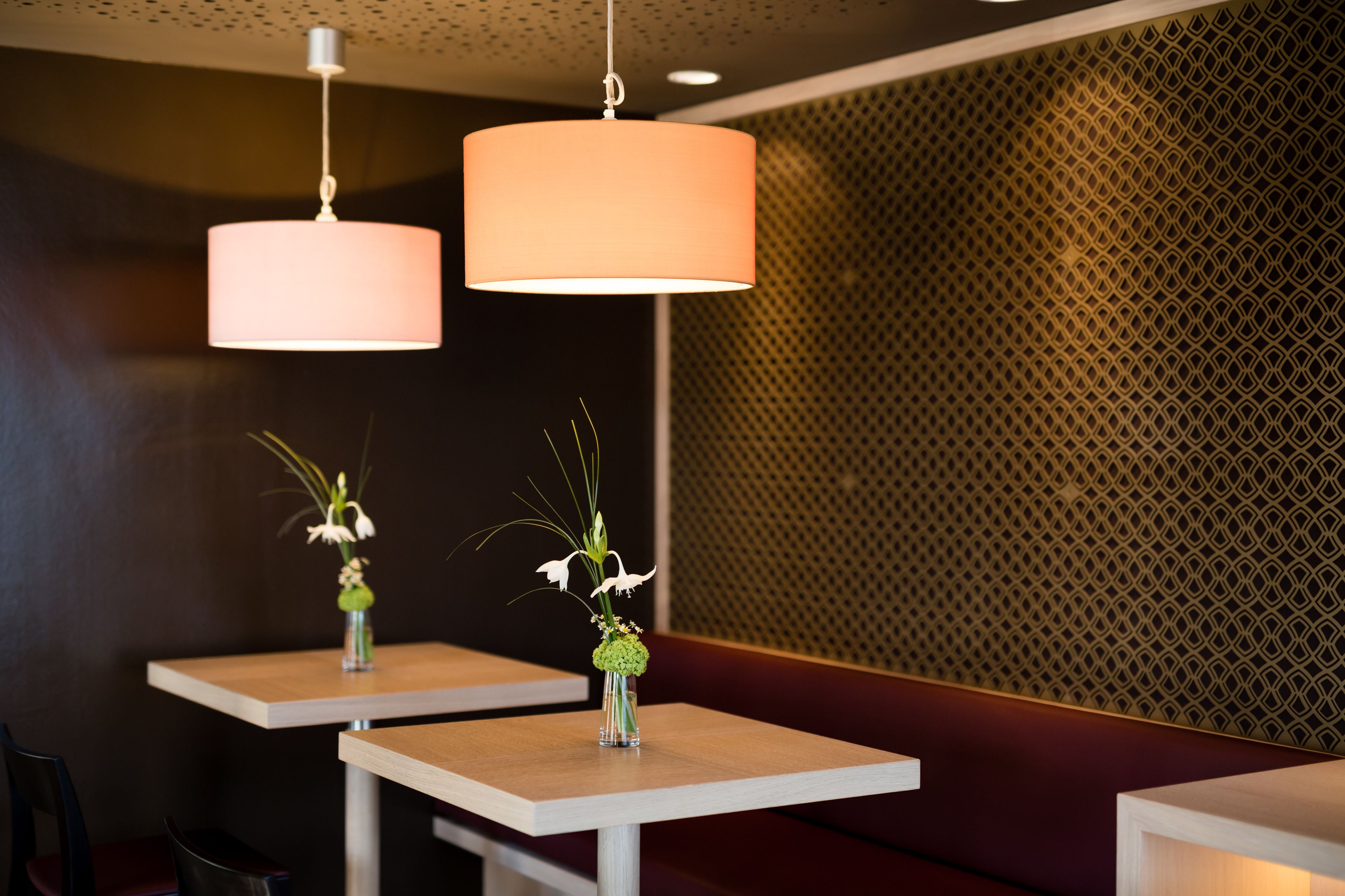 Interno di un ristorante con due tavoli quadrati, ognuno decorato con un vaso di fiori.
