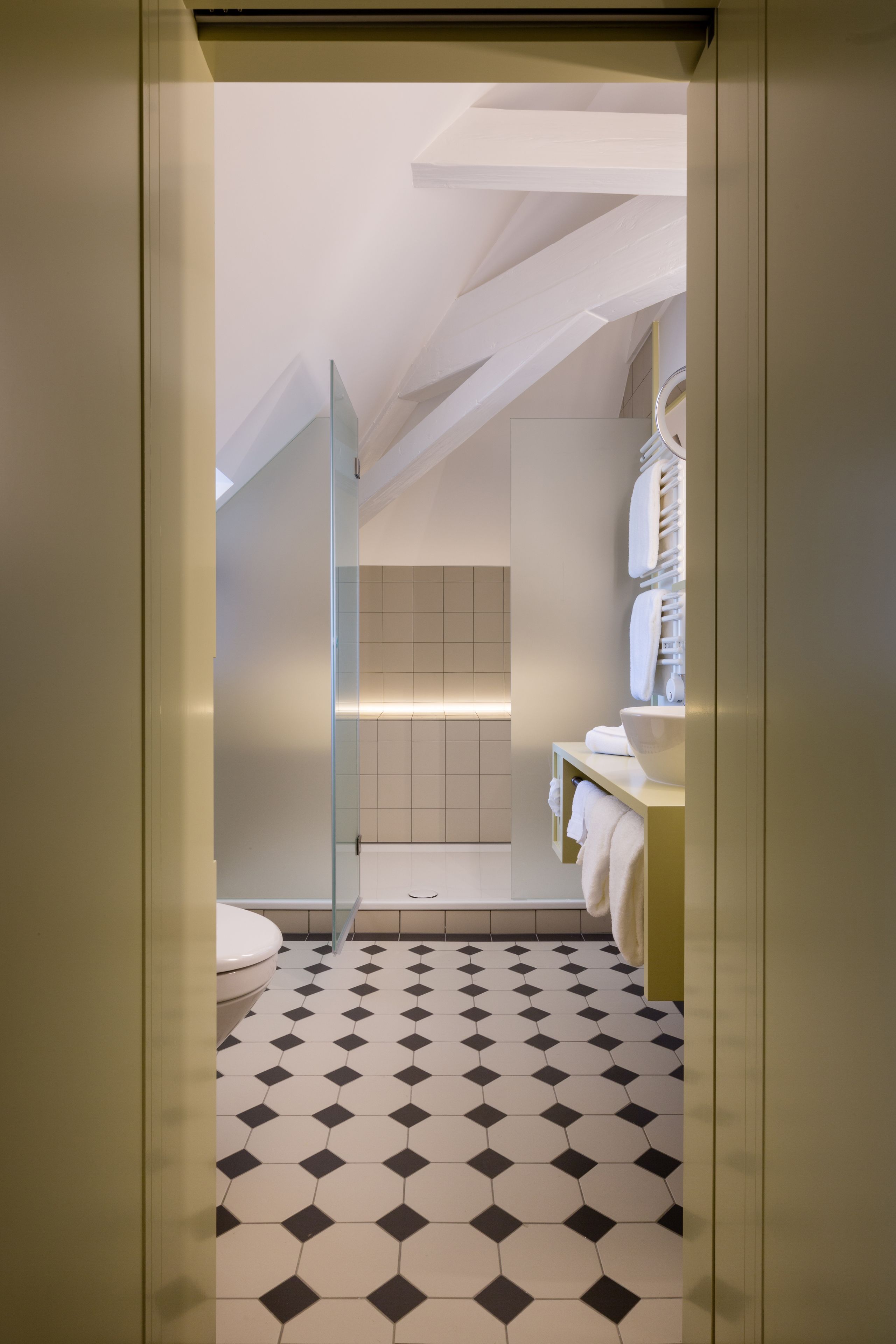 Une salle de bain moderne avec un carrelage au motif géométrique, une douche en verre et un lavabo blanc doté d’un porte-serviettes.