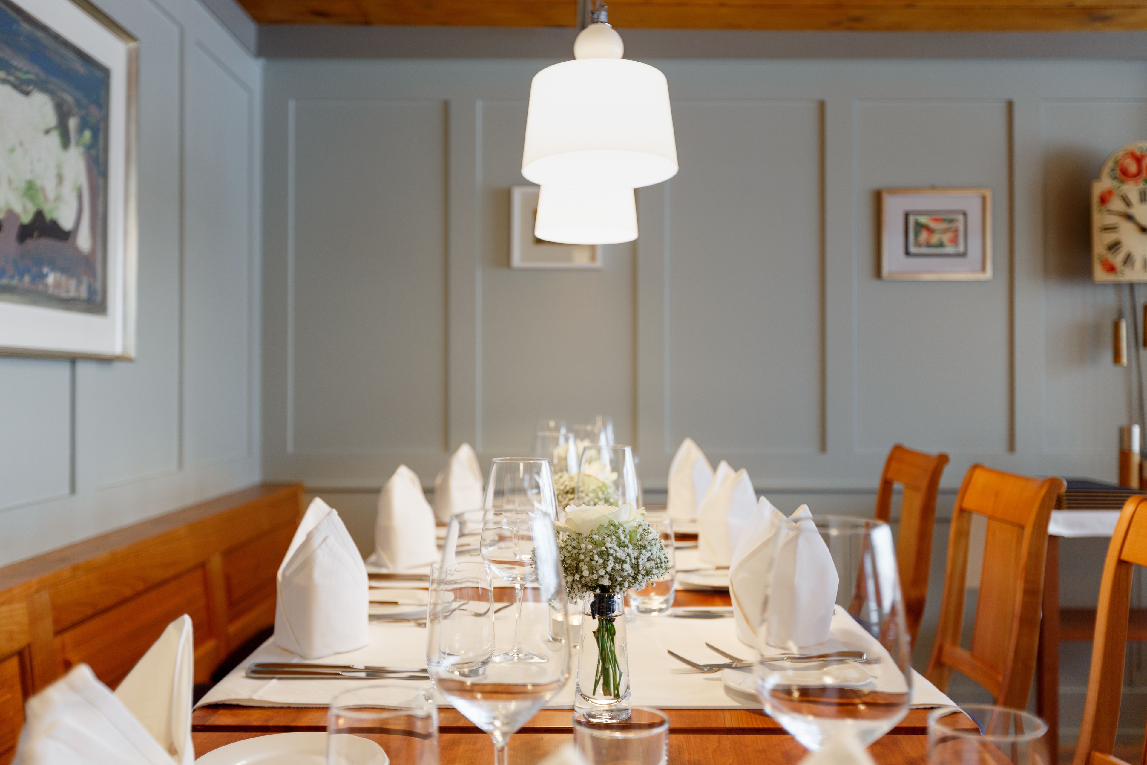 Una mesa de comedor dispuesta con servilletas blancas, copas de vino y un pequeño florero con flores.